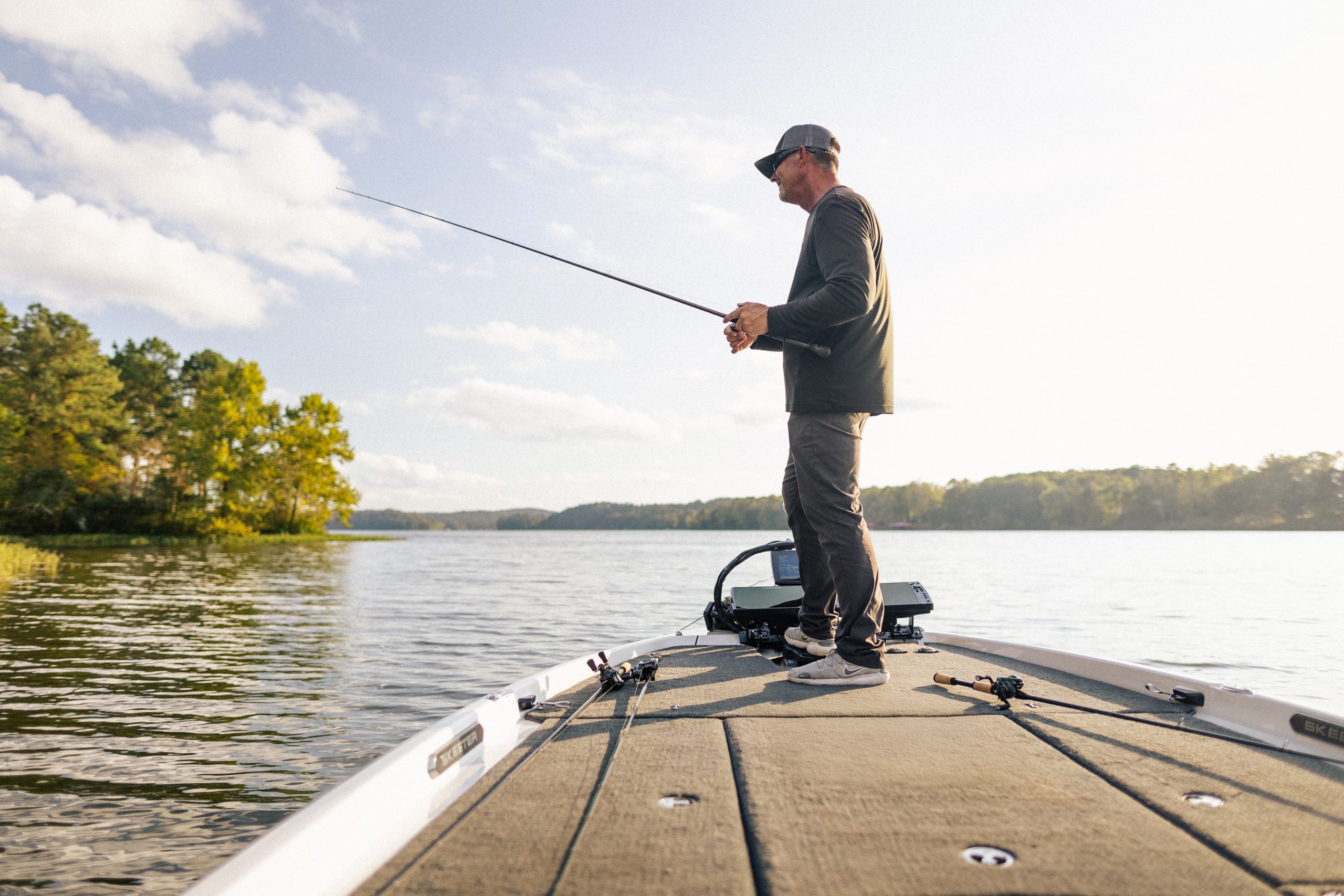 Angler fishing from the bow of a bass boat at sunrise demonstrating fishing rod performance and technique